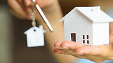 Hand holding a small model of a house and another hand holding a key