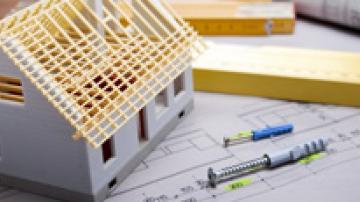 Model home sitting on blueprint papers beside a ruler and pens